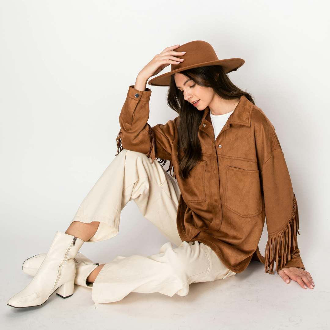Woman wearing a brown suede jacket, hat, and white boots on a light background